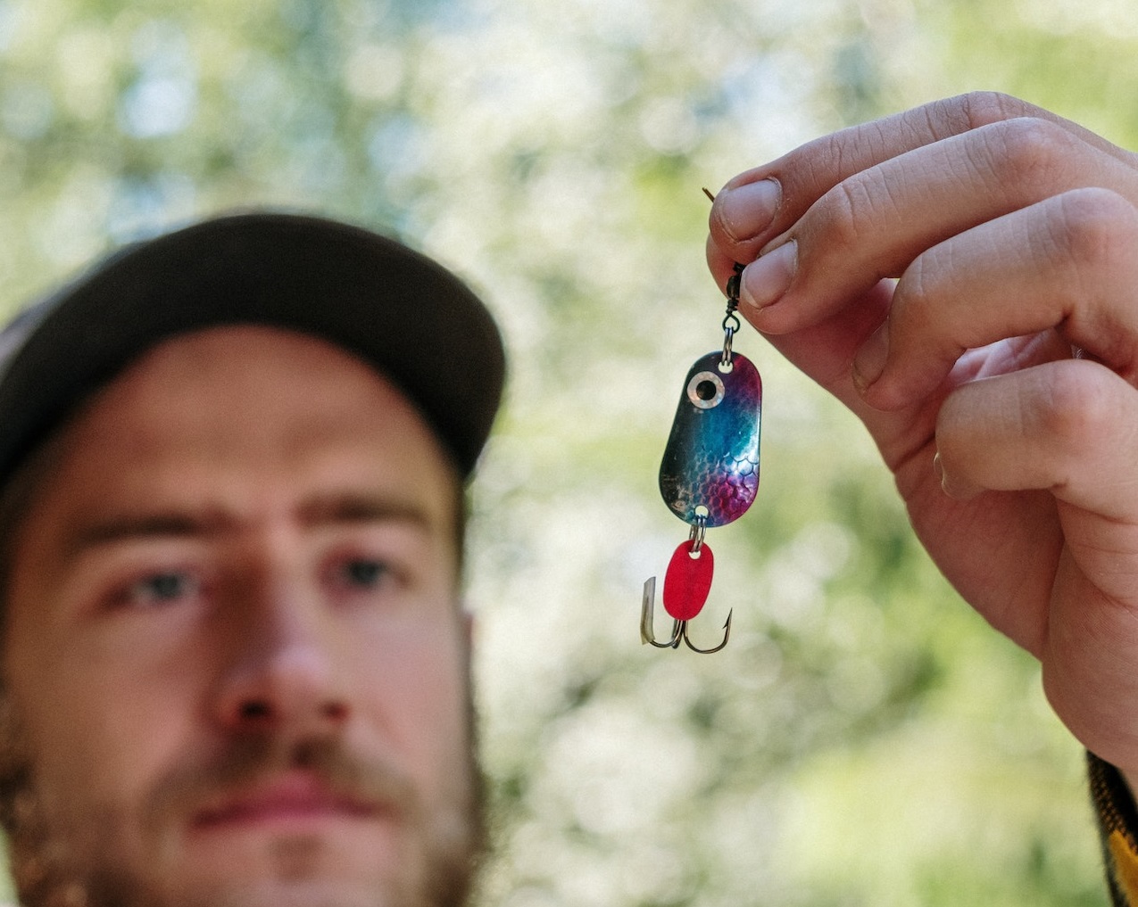 Man wearing jacket and hat is holding blue and silver beaded fishing lures.
