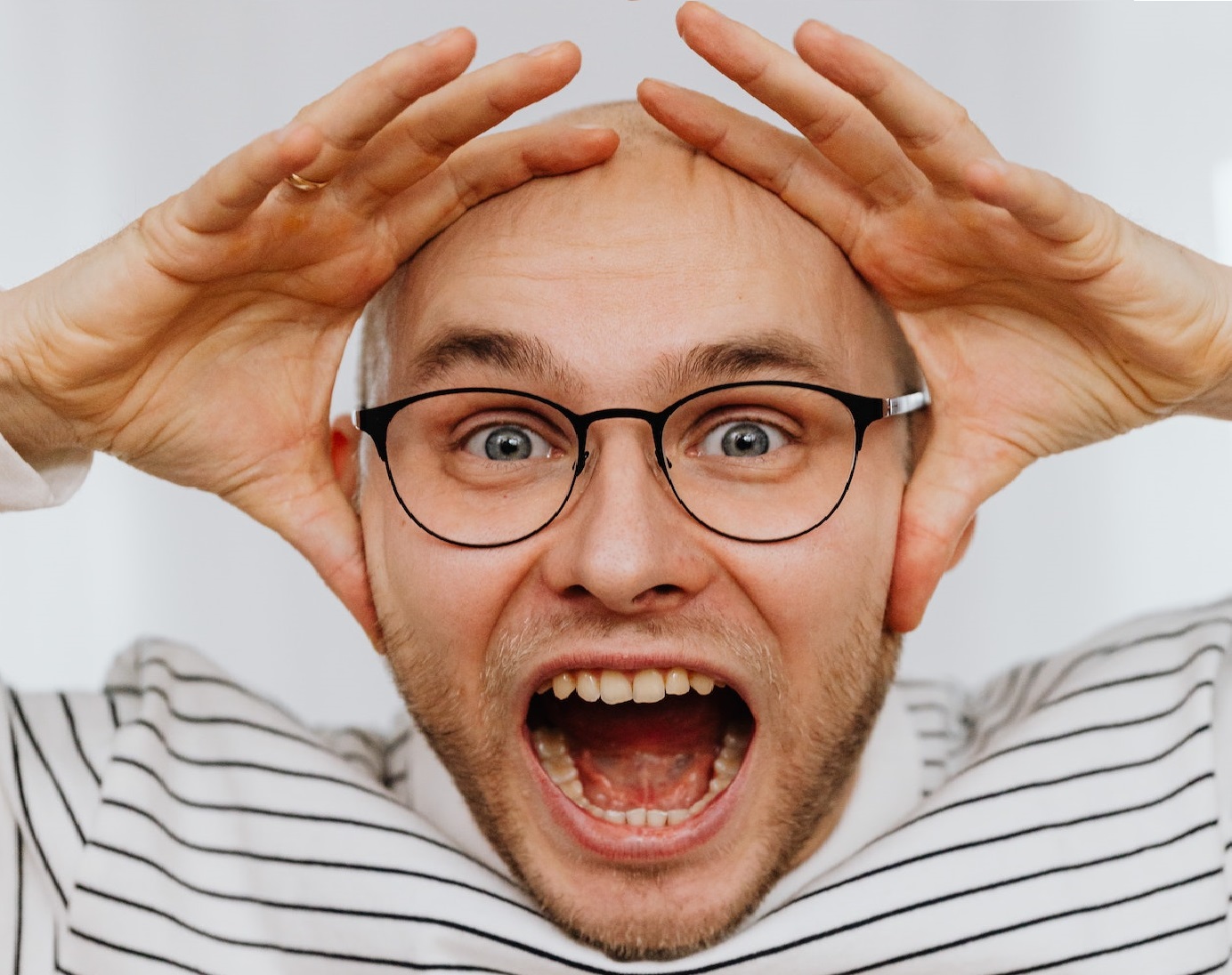 Man wearing shirt and glasses is screaming at camera.