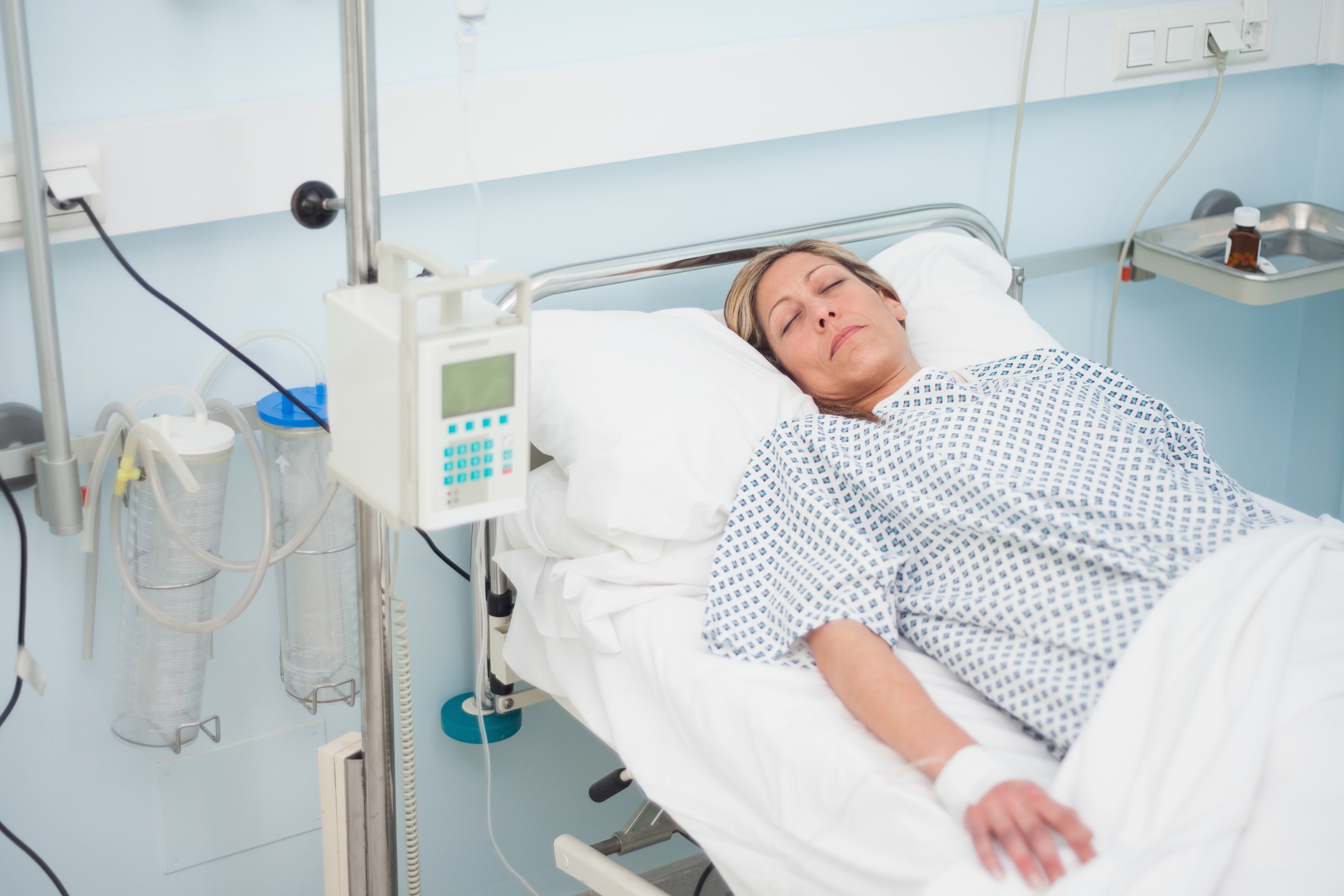 Woman lying on a medical bed with closed eyes in hospital ward.