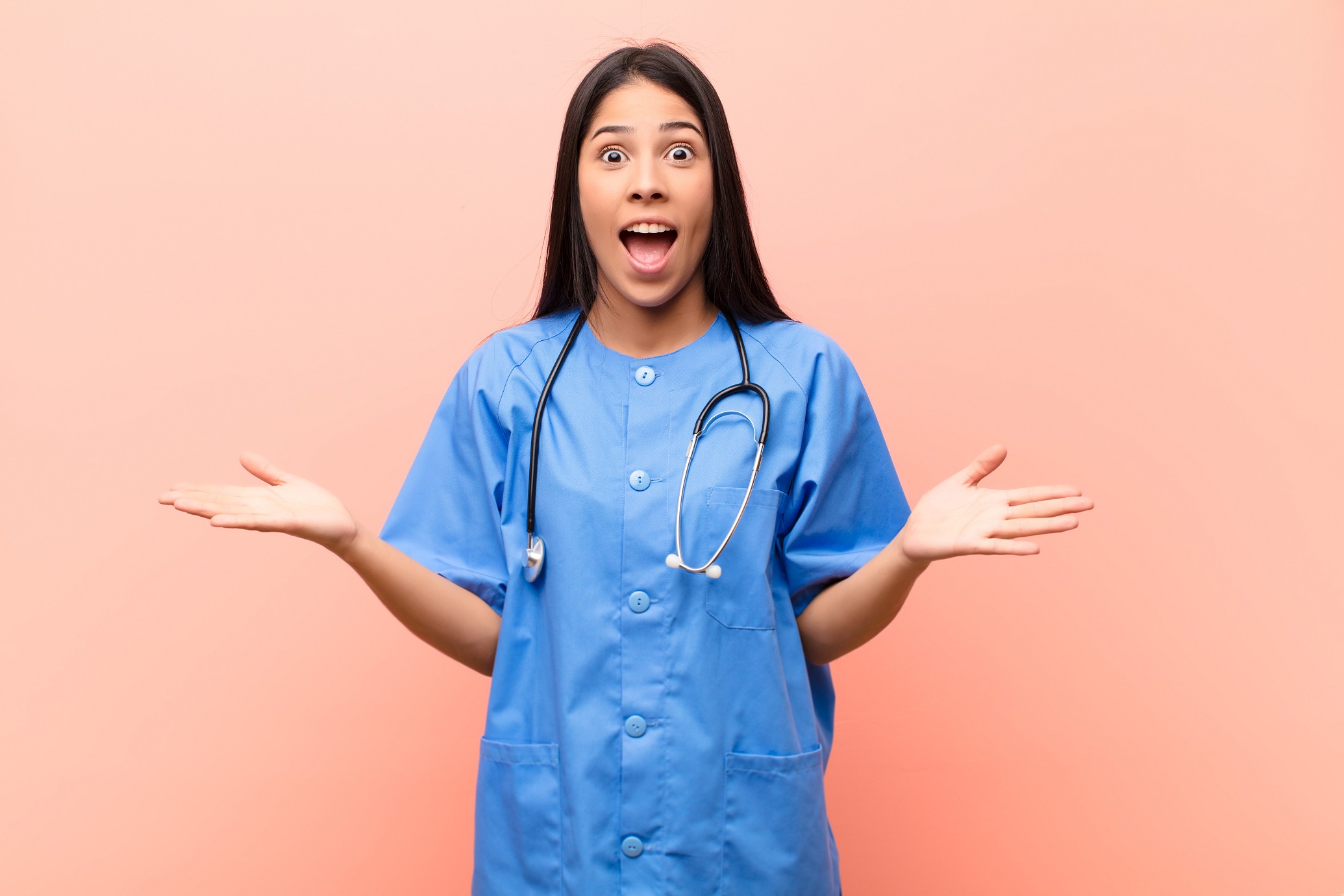 Young nurse feeling surprised, smiling against pink wall.