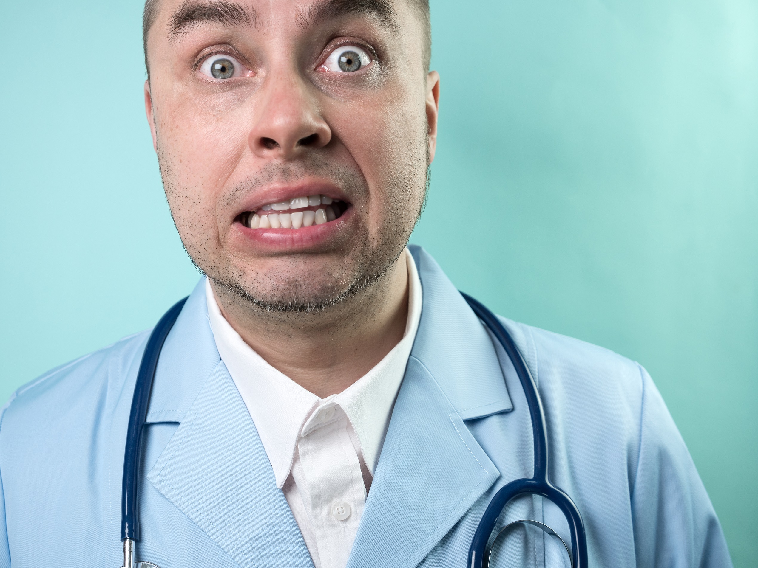 Doctor wearing blue medical suit with stethoscope, looking shocked.