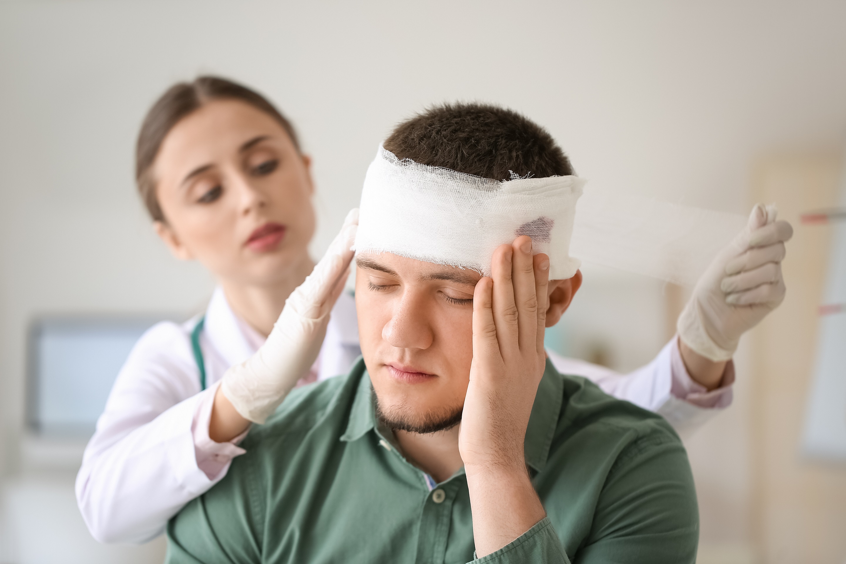 Woman doctor applying bandage onto head of young man in hospital.