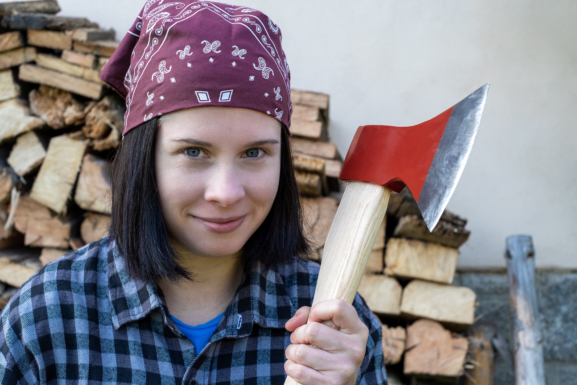 Woman stands and looks at the camera, holding an hatchet.