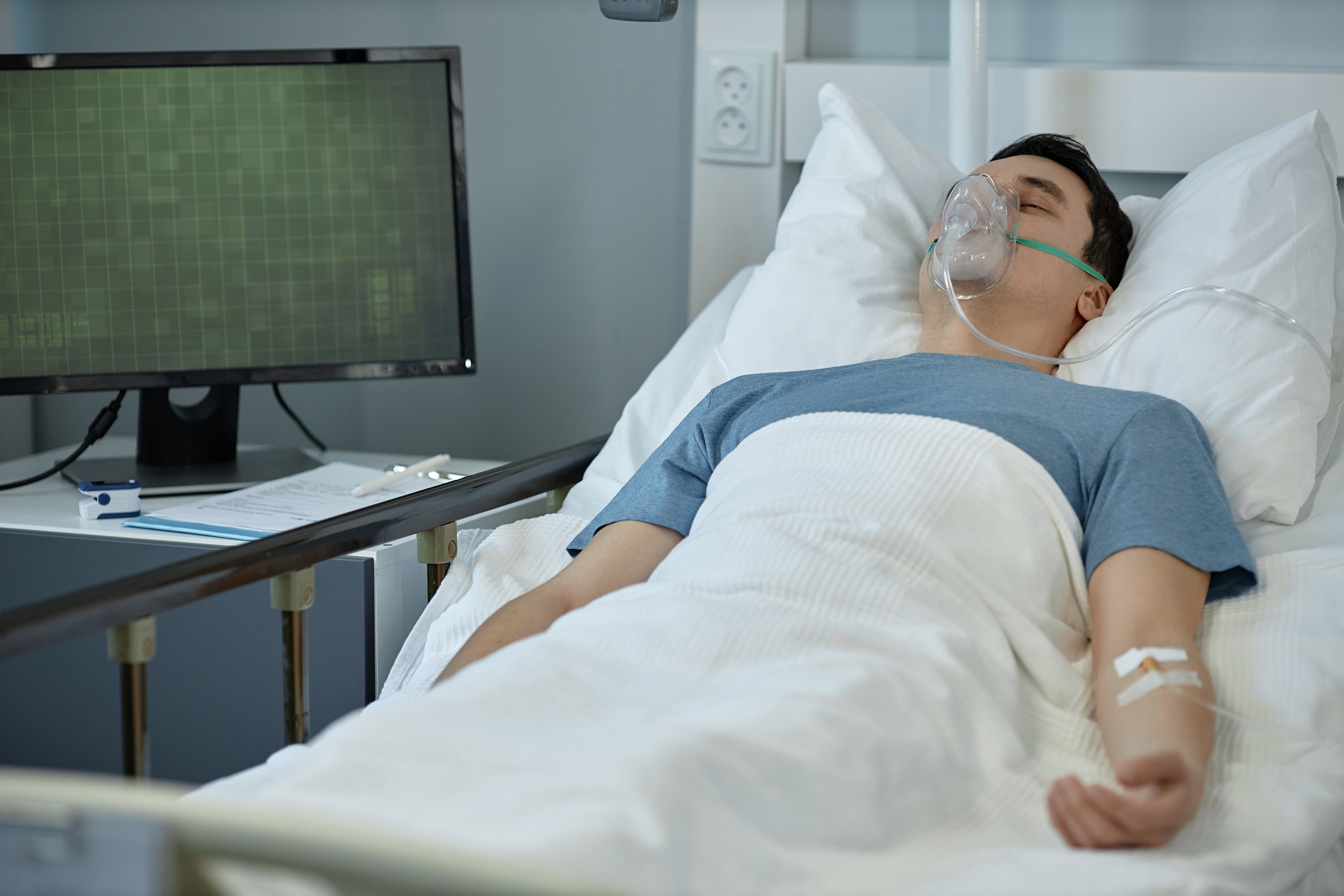 Young man lying on hospital bed with oxygen mask on.