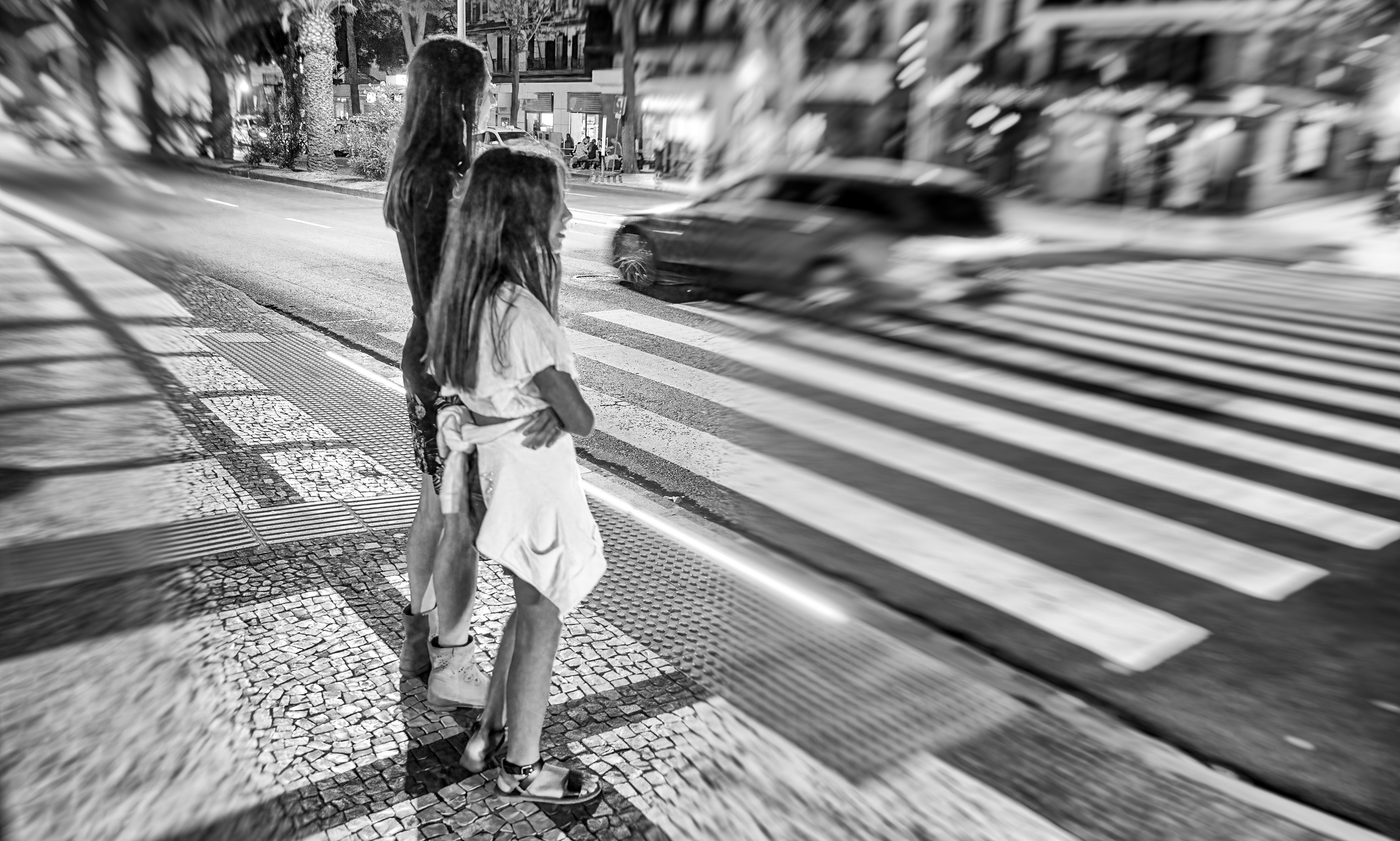 B&W photo of woman with her daughter crossing main city street at night.