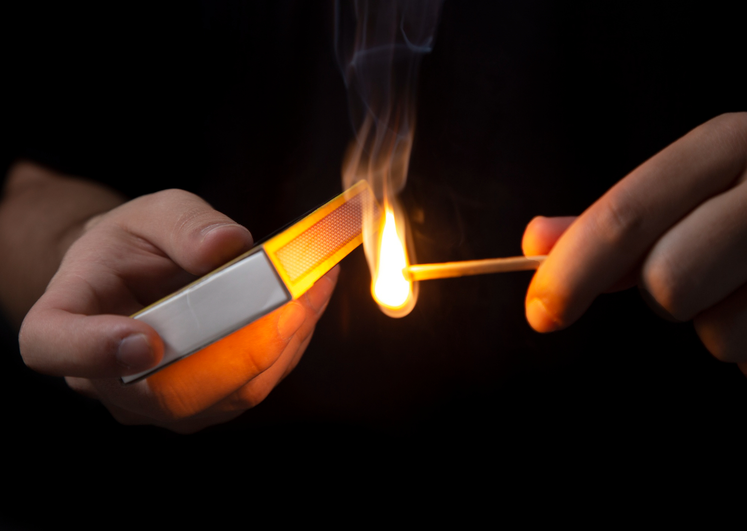 Hands igniting match on a black background.