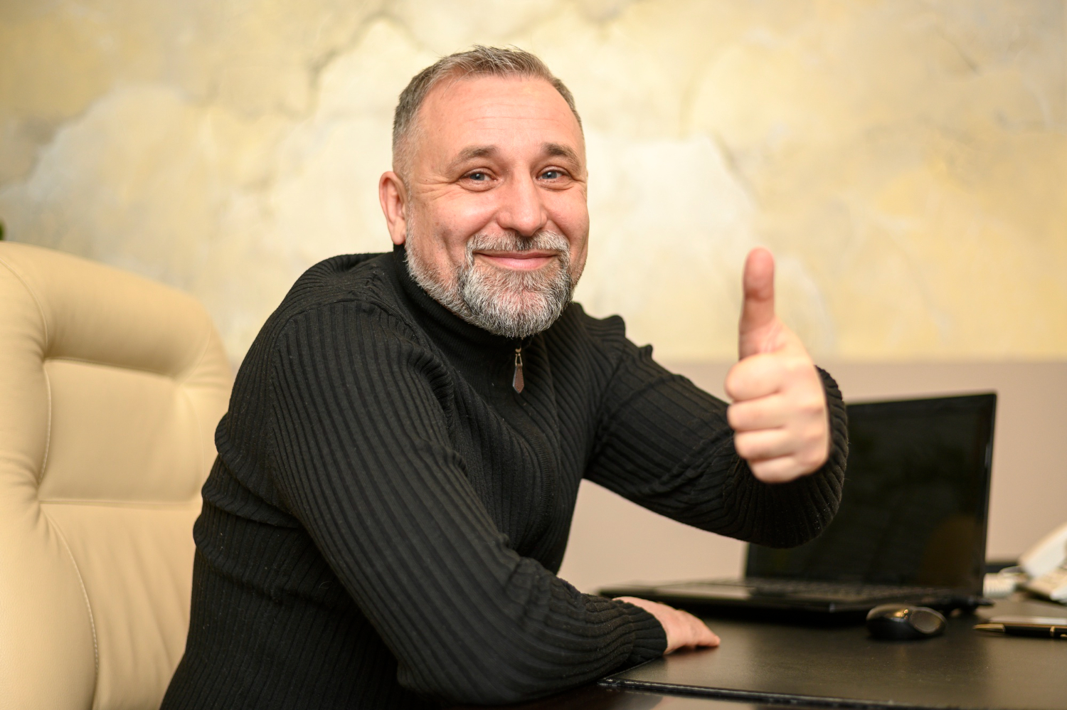 Man seating on the desk by his PC making a thumbs up.