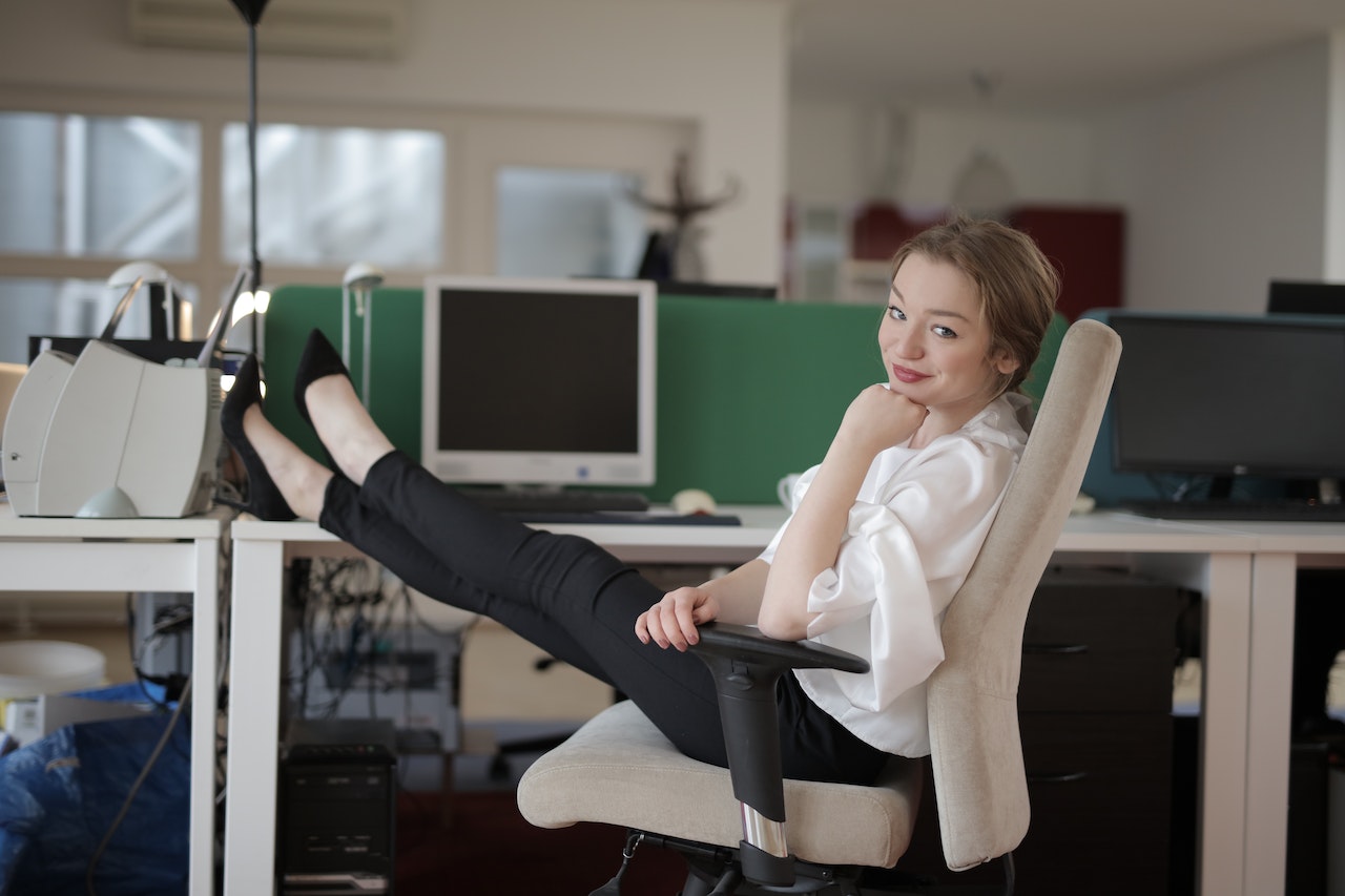 Young elegant woman is smiling with feet on table in the office.