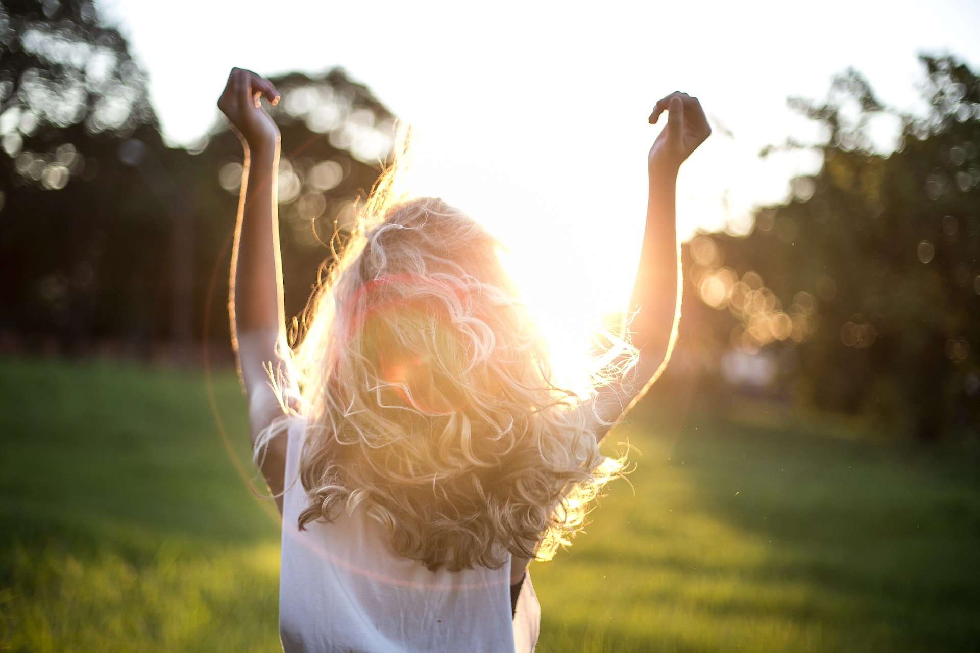Blond woman with hands in the air looking at the sunset looking happy in nature
