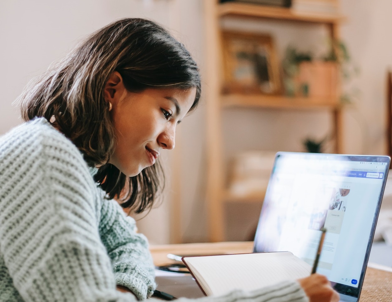Young student is taking notes while using laptop.