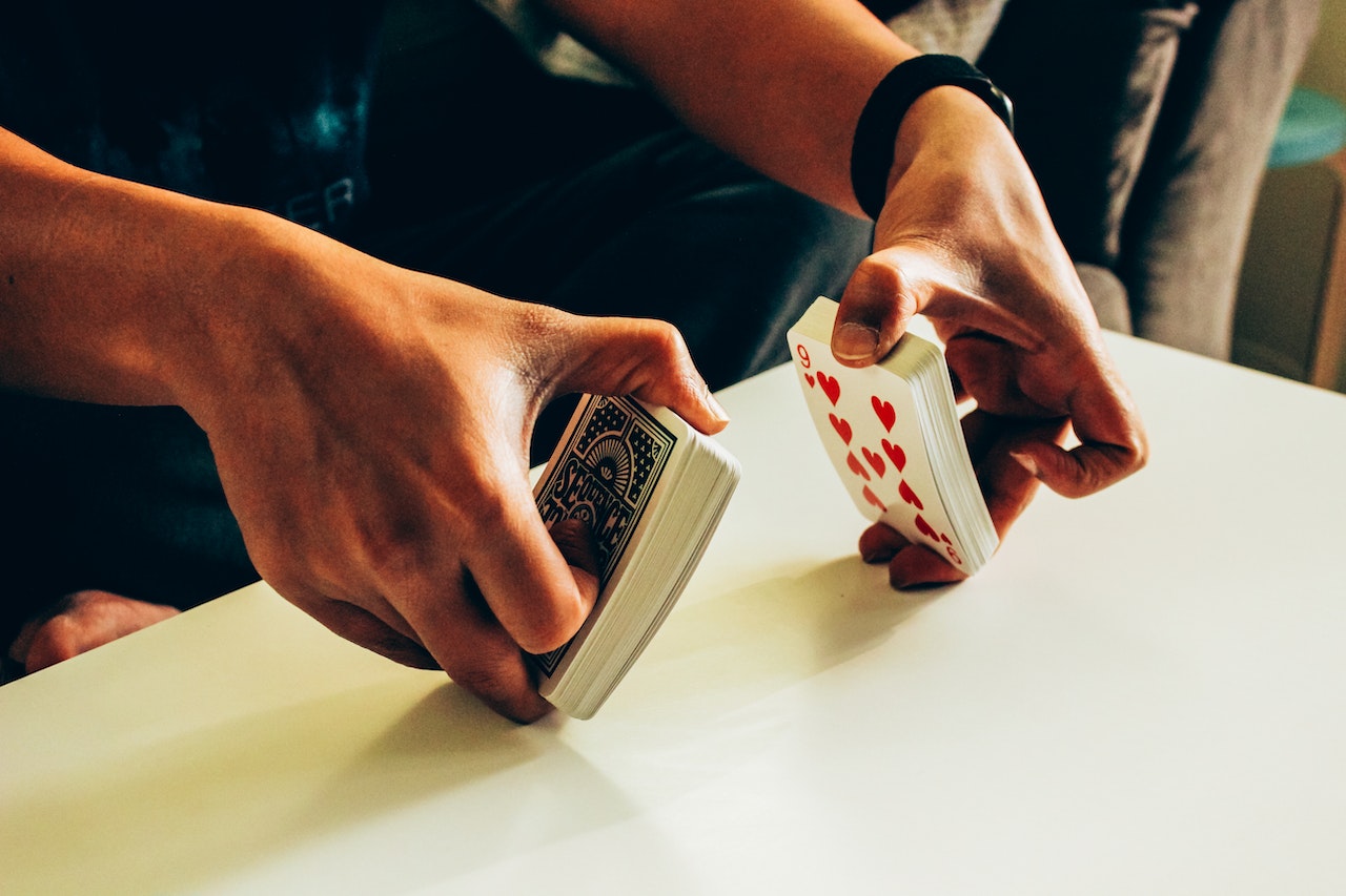 Person wearing blue shirt and jeans is shuffling cards on a white table (close up photo).