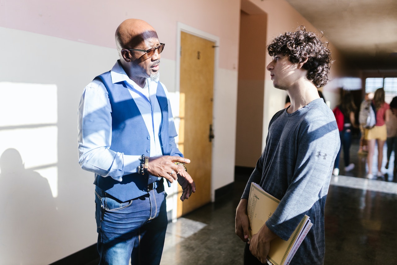 A teacher is talking to his student in school hallway.
