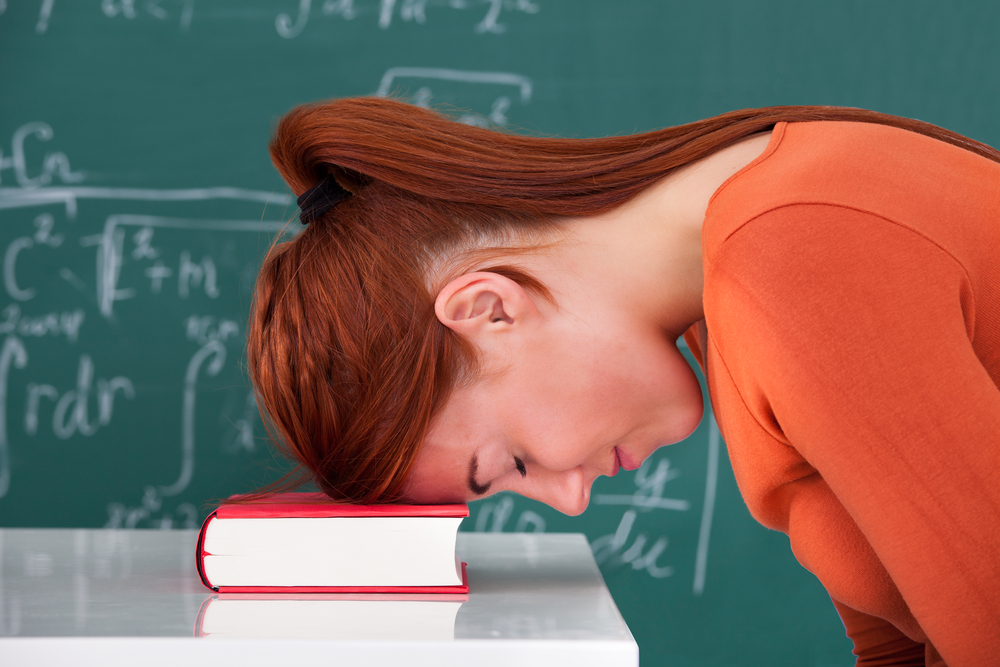 Side view of sad young female teacher leaning head on book