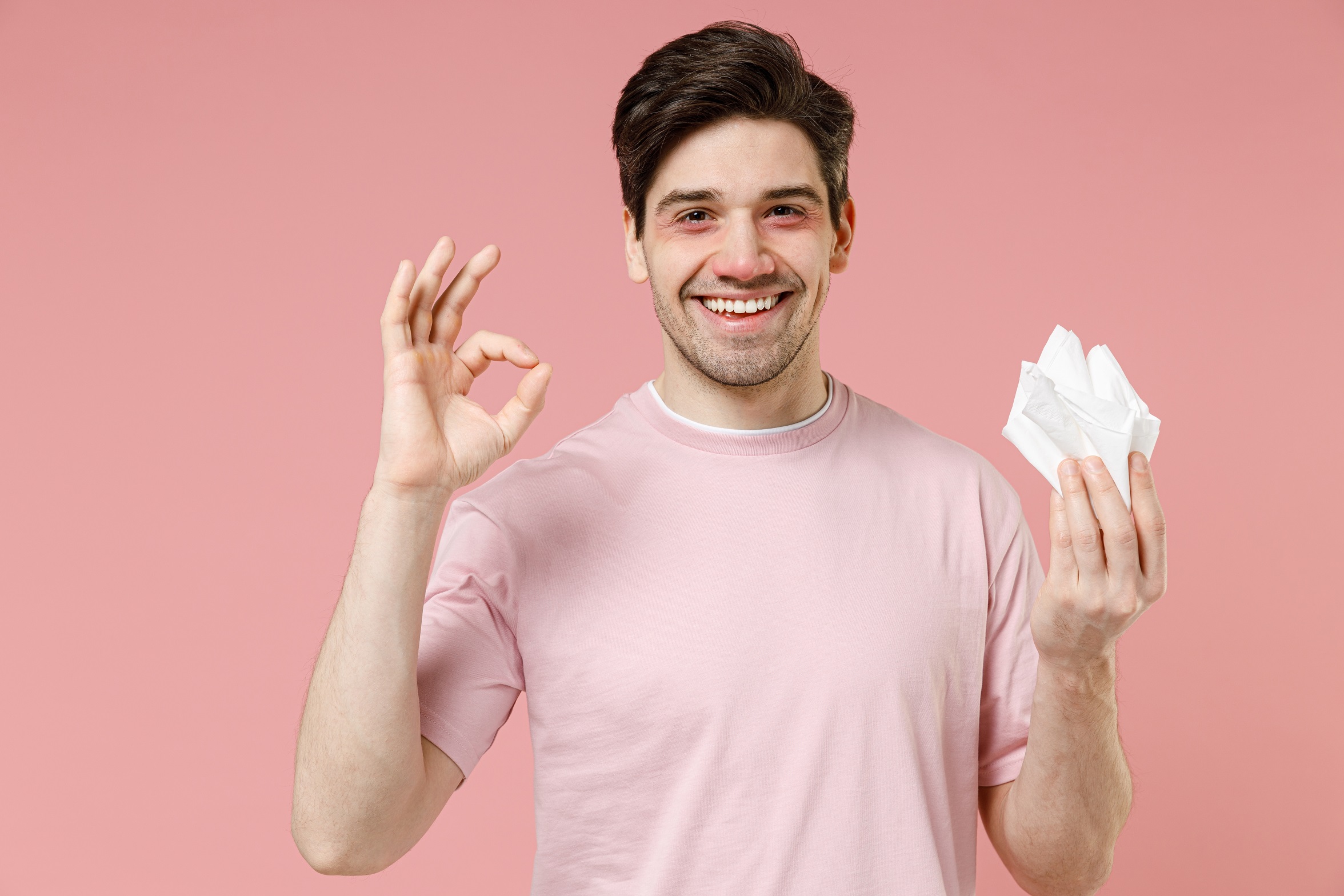 Young man is holding paper napkin isolated on pink background.