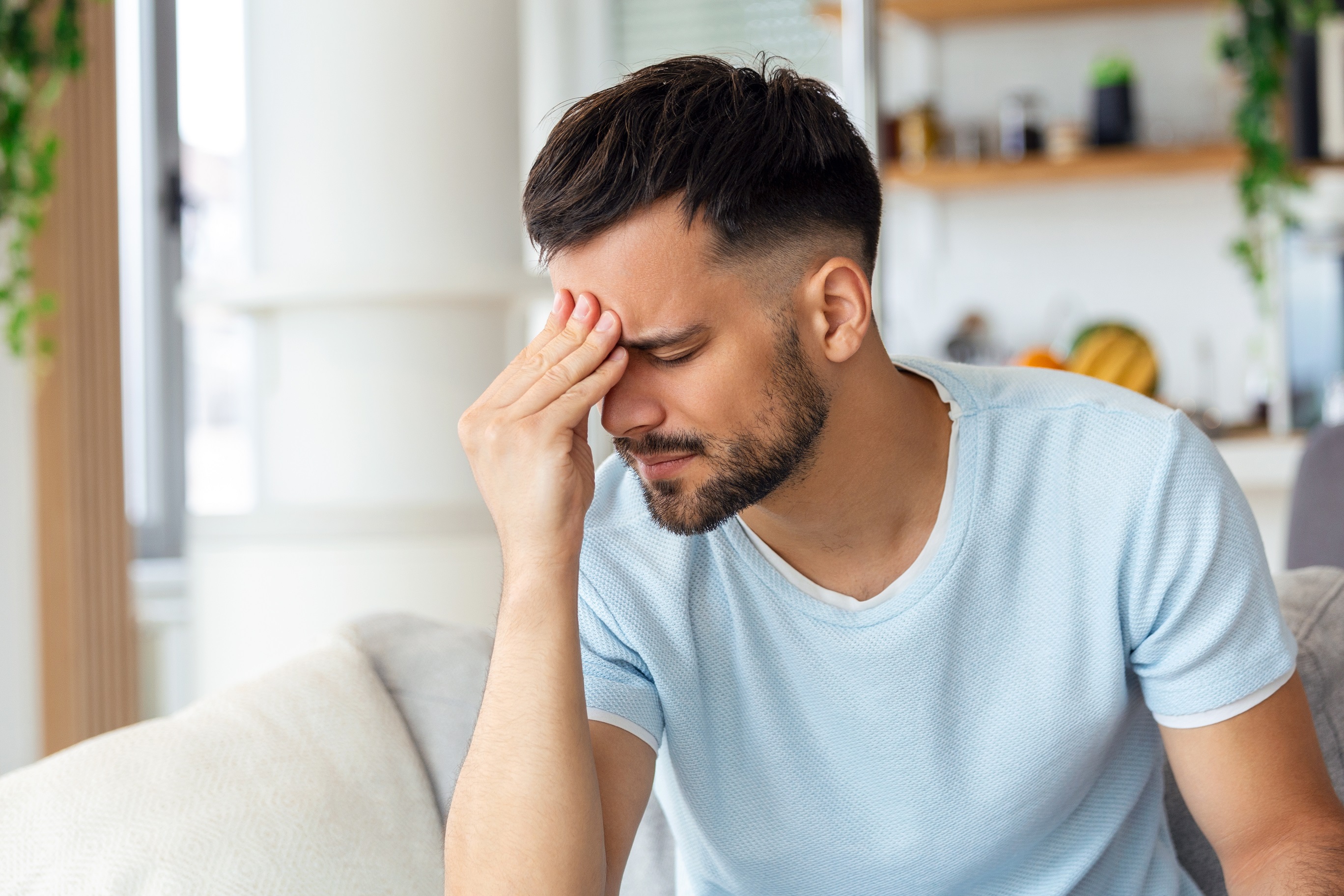 Frustrated young man touching his head and keeping eyes closed.