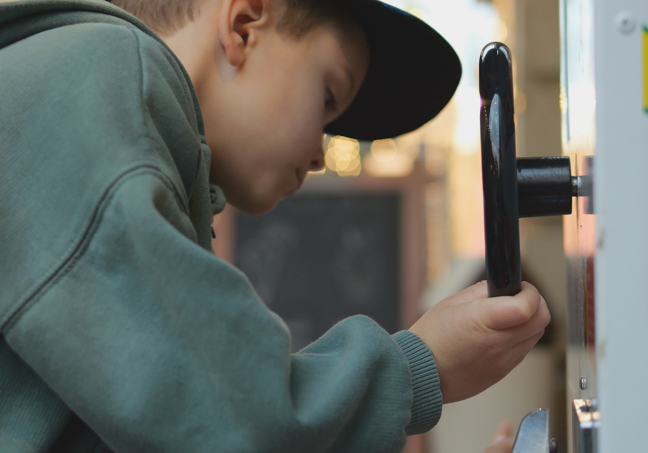 Boy in green zip sweatshirt and cap reaches for won prize.