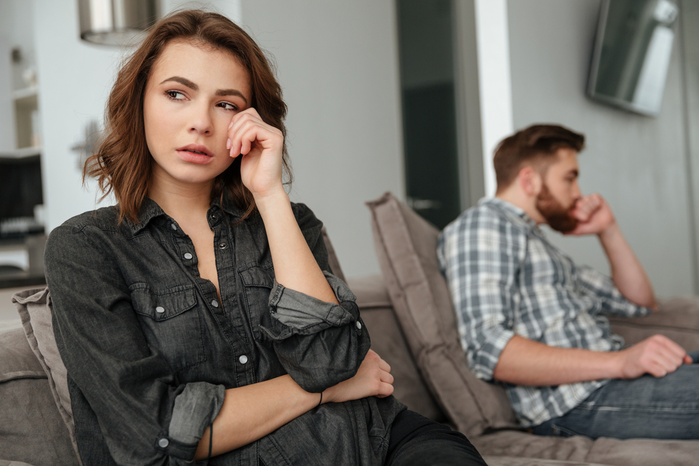 Photo of young sad couple sitting on sofa indoors