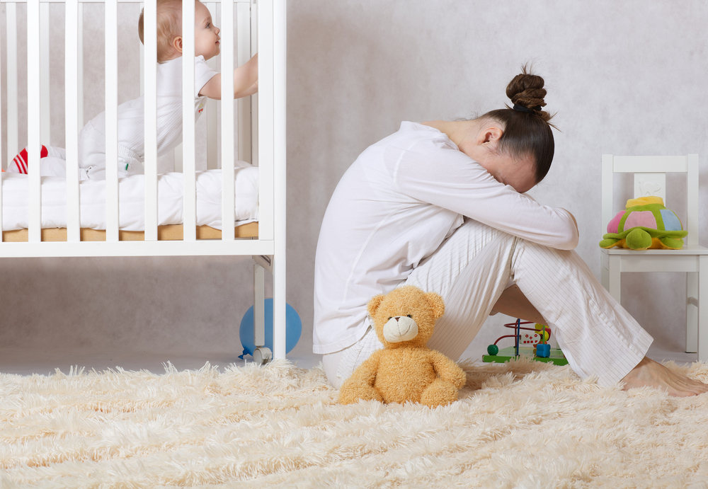sad Young mother sitting next to baby's bed