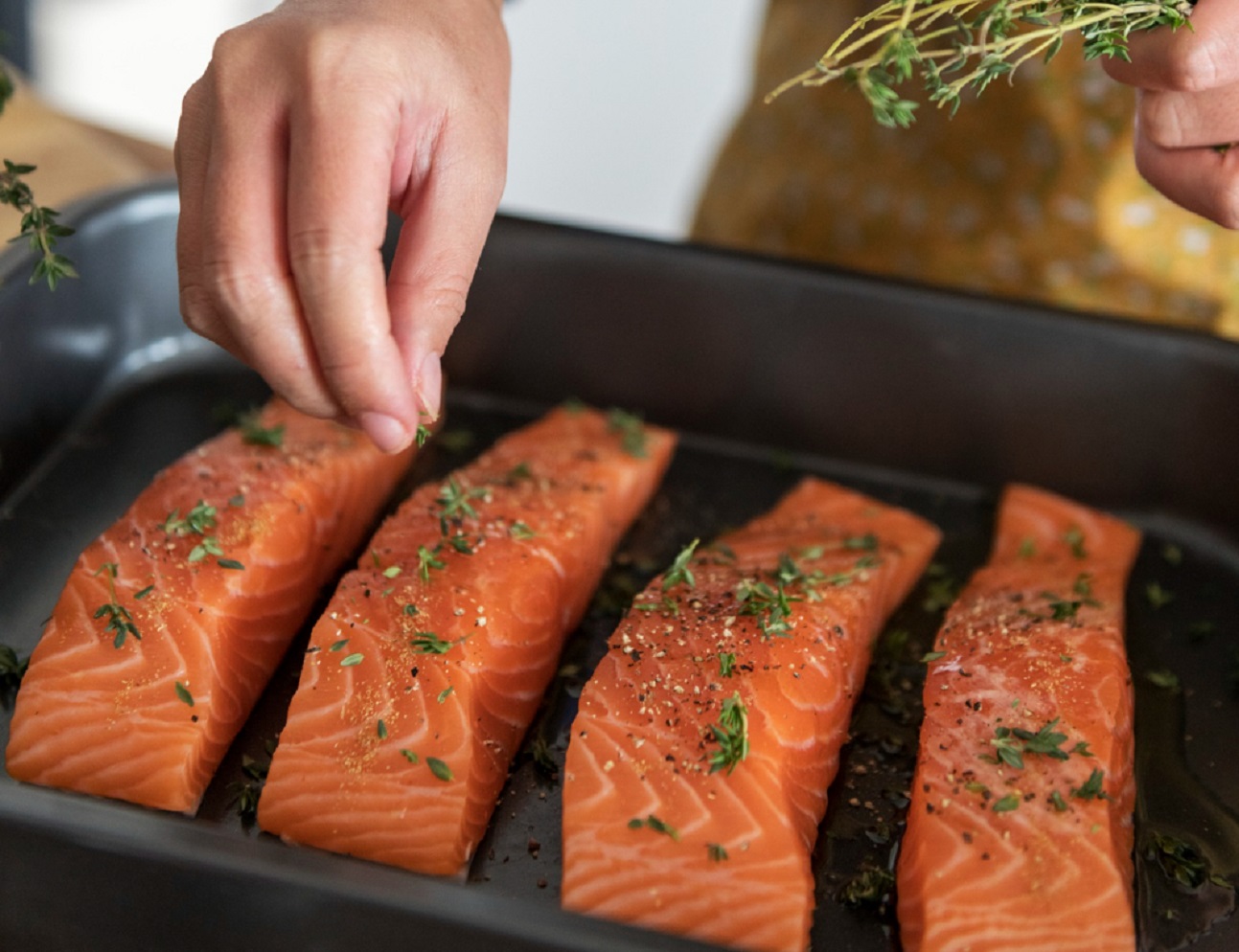 Woman adding spices and herb to raw salmon.
