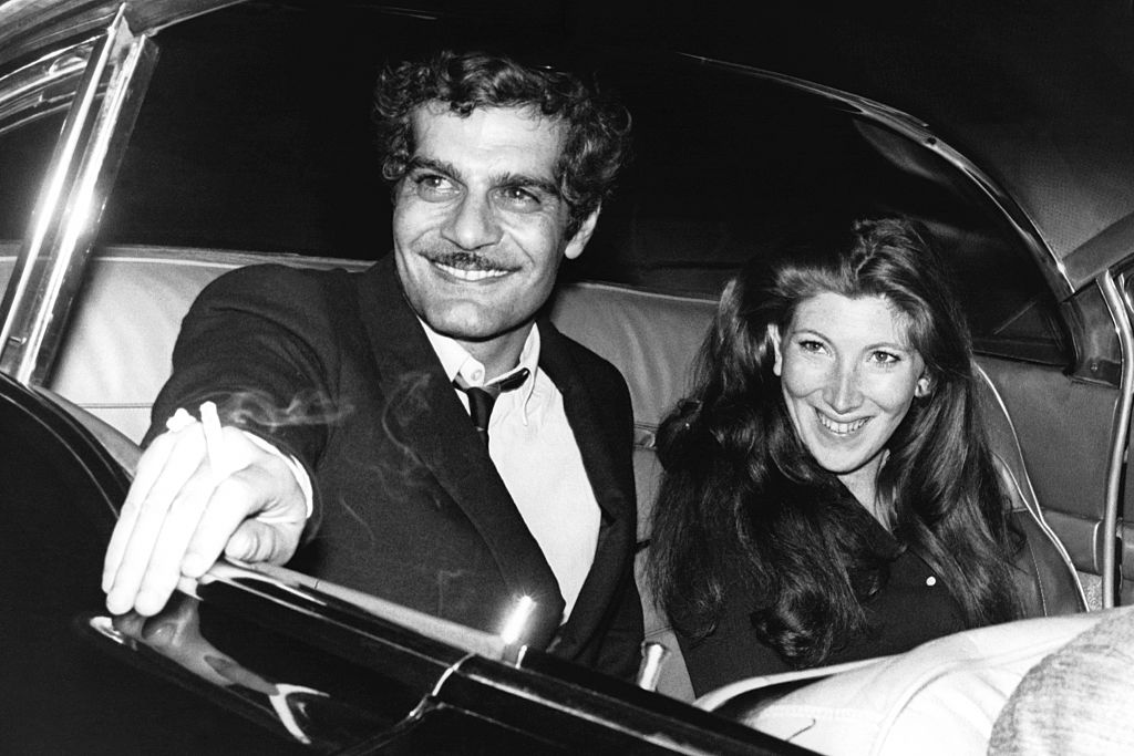 Egyptian actor Omar Sharif in the back of a car alongside a dark-haired lady, circa 1960