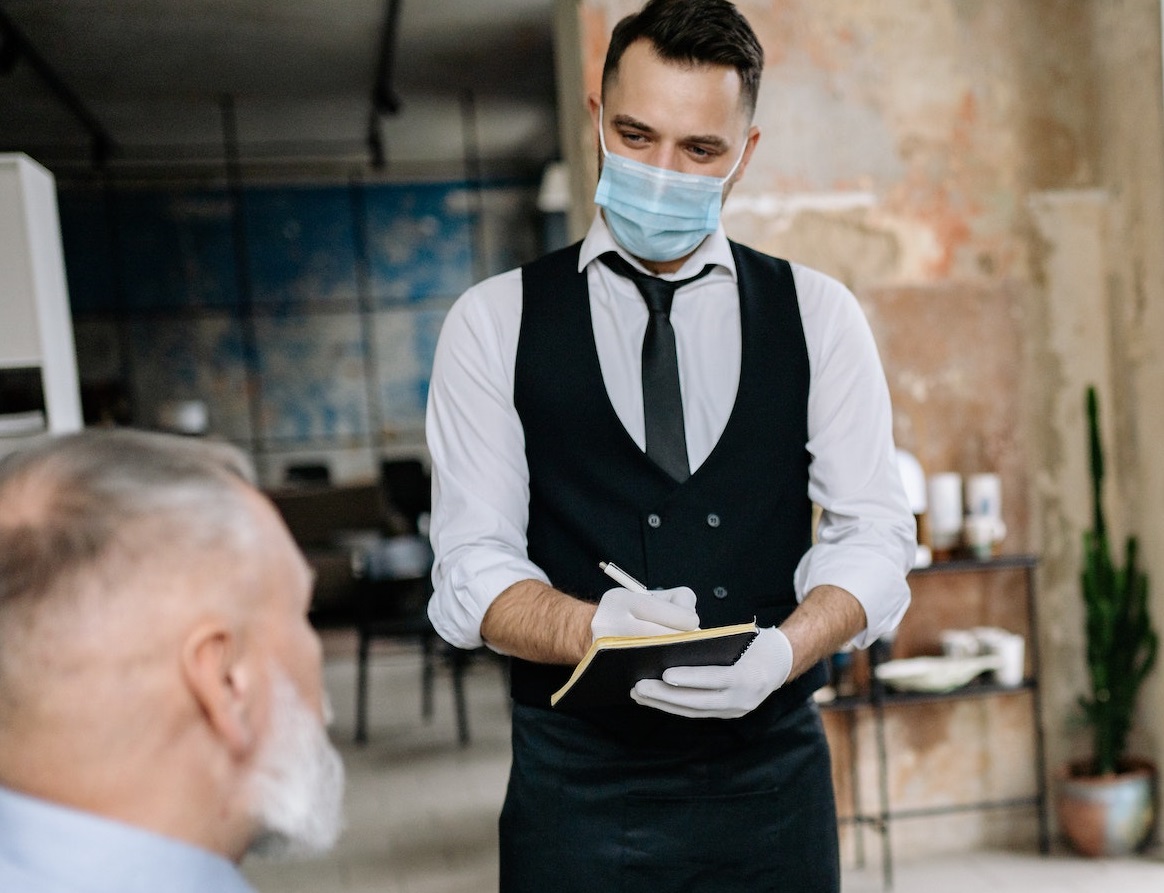 Waiter with mask is talking with a costumer in restaurant.