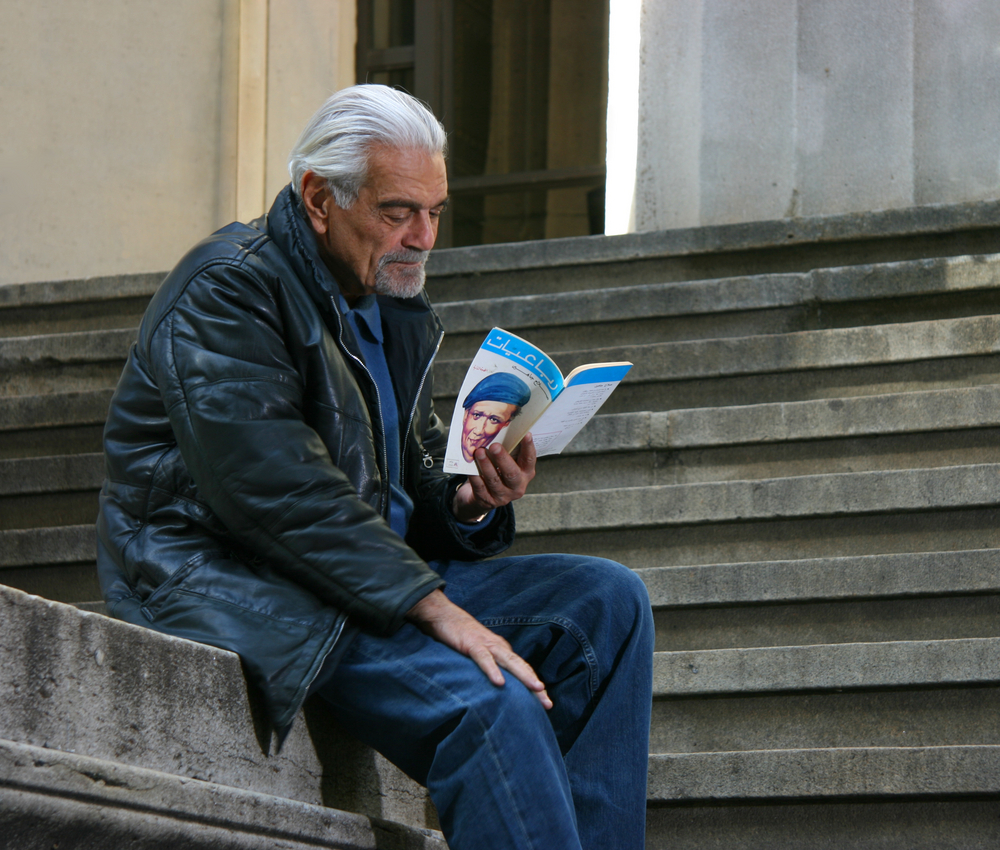 Omar Sharif during shooting in Wall Street, New York sitting on stairs reading a book