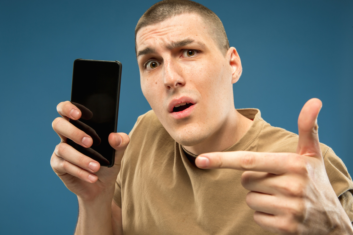 Man is holding a cell phone in hand and looking surprised.
