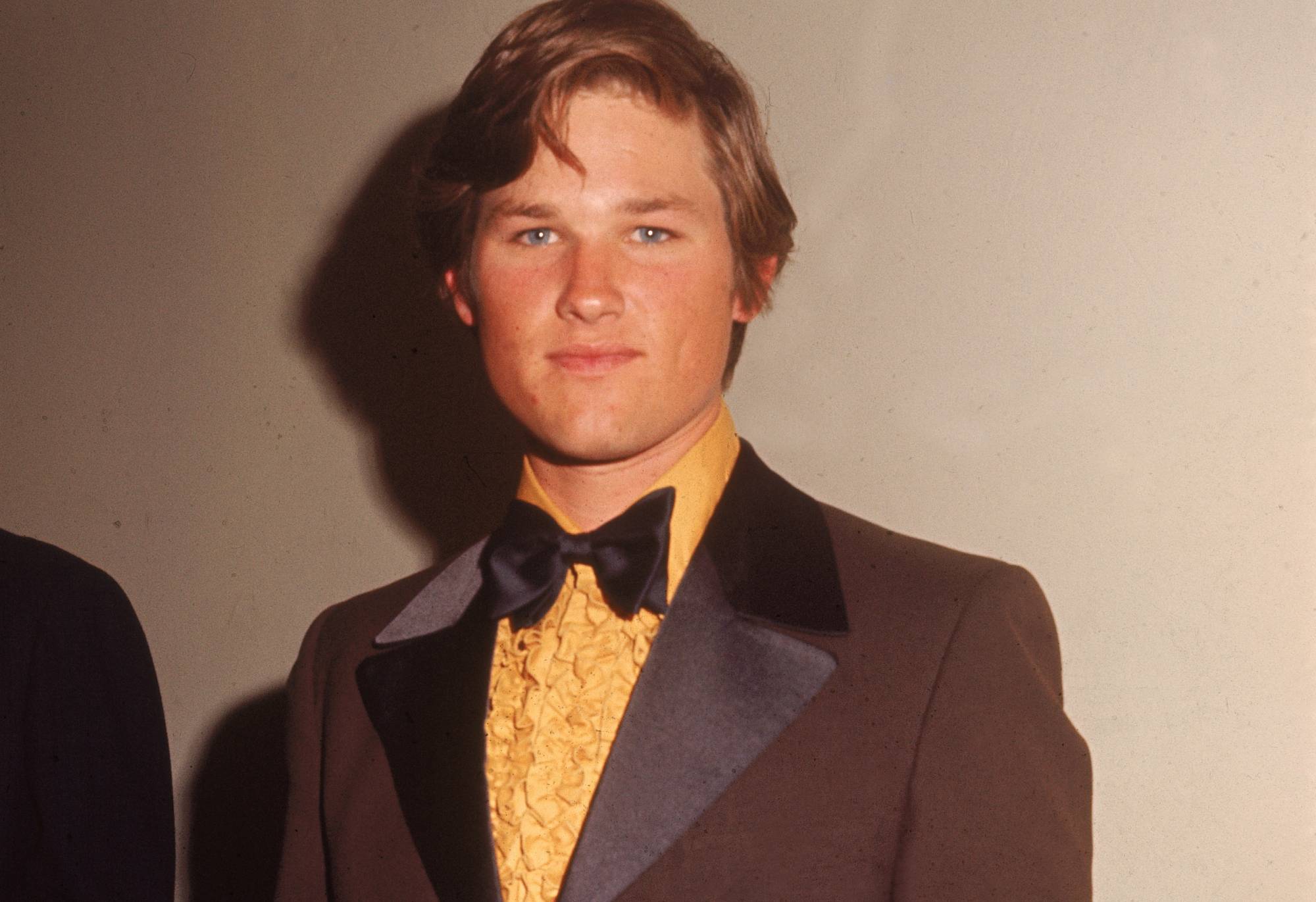 American actor Kurt Russell waring a brown tuxedo with a yellow ruffled shirt, 1970s.