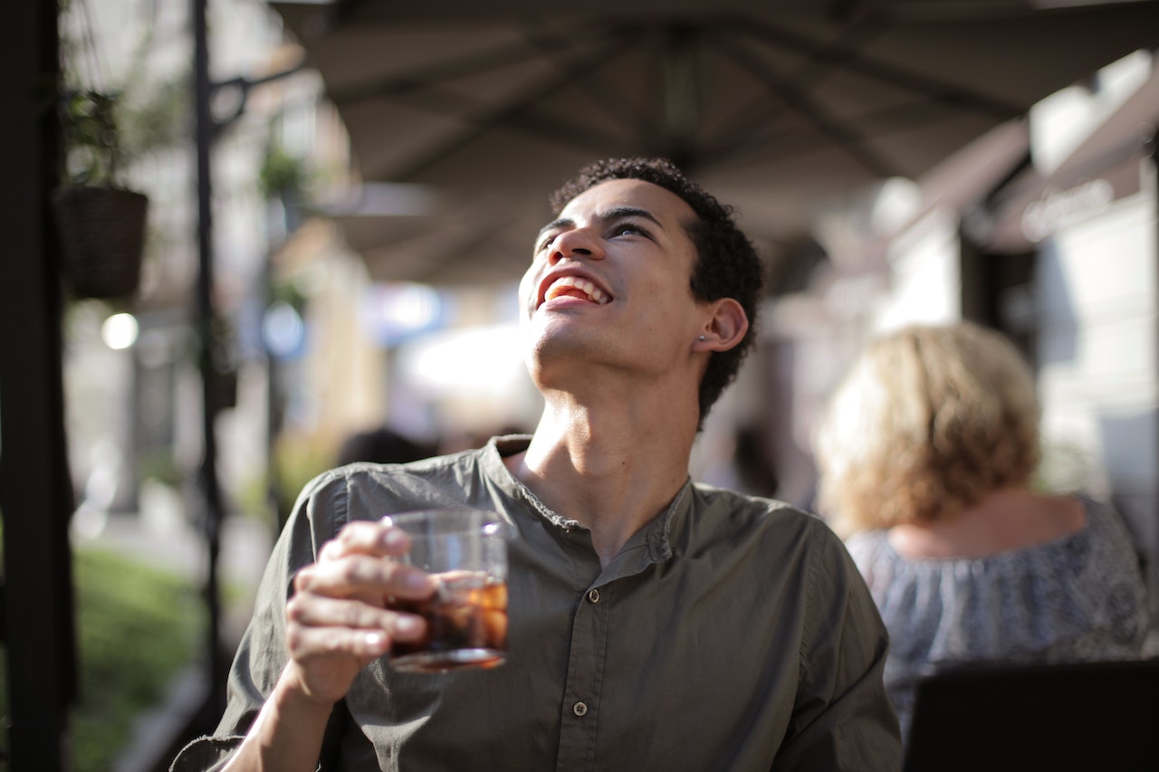 Man wearing grey shirt is drinking ice tea at restaurant.