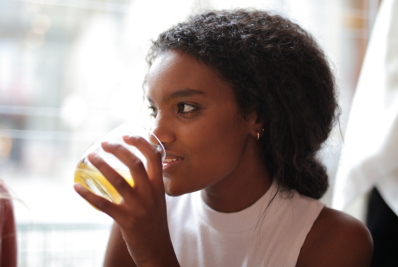 Woman is drinking lemonade from the glass and looking at side.