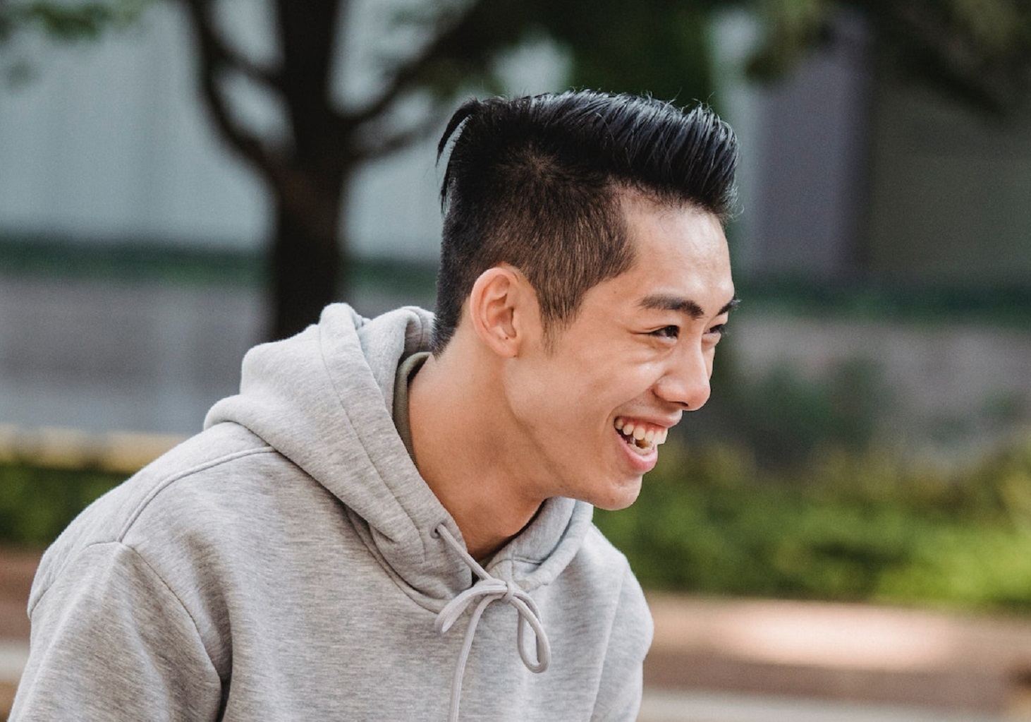 Young asian man is sitting outside and laughing.