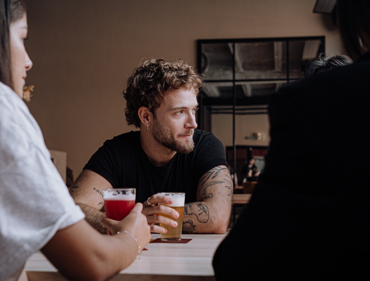 Young people are seating inside at bar and drinking beer.