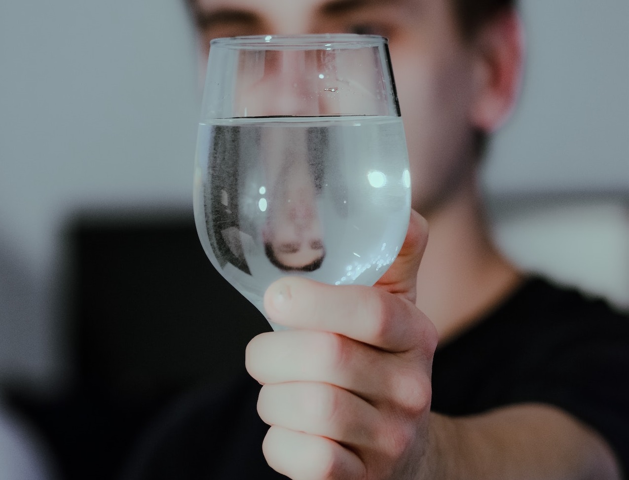 Man with black shirt is holding a glass with water in front of him.