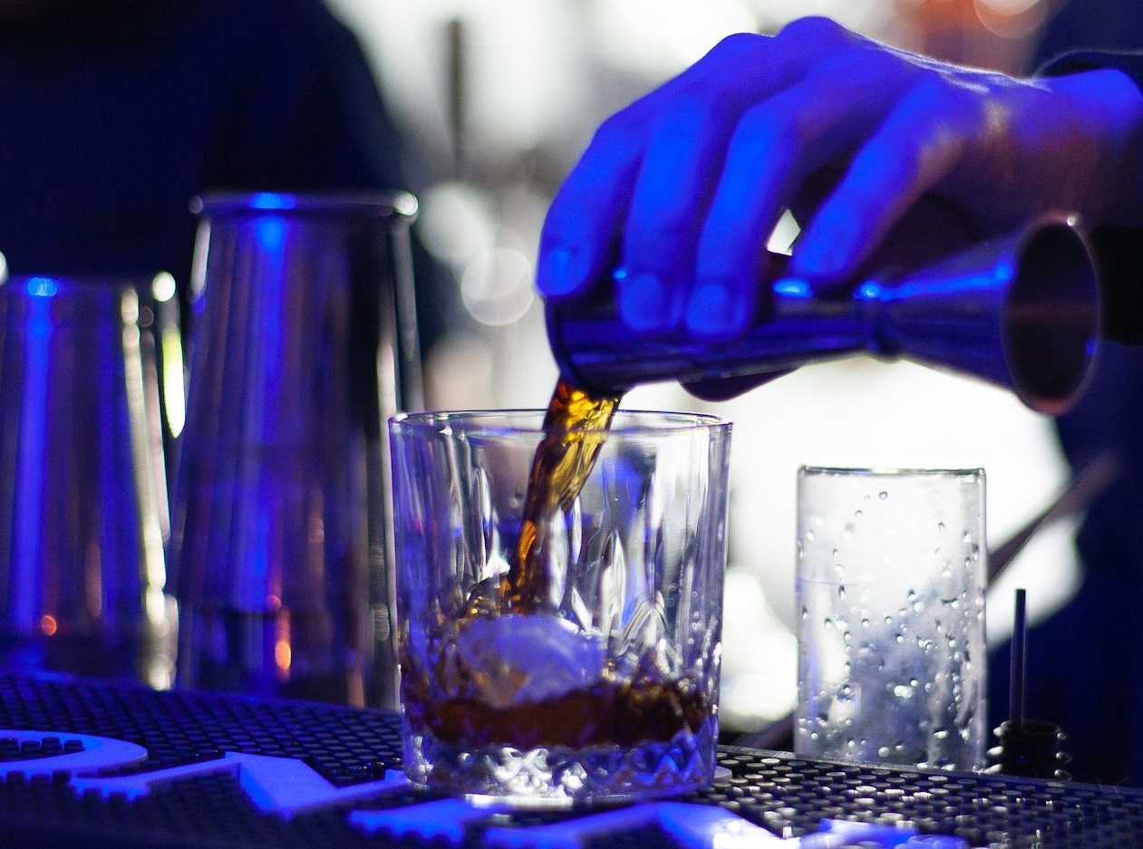 Bartender is pouring a drink to a glass.