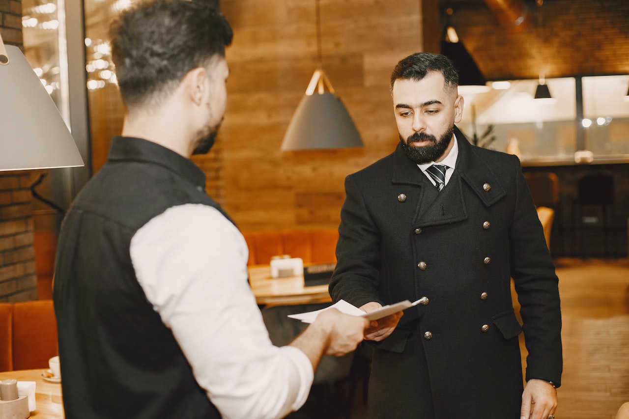 Man is giving a paper to a waiter at restaurant.