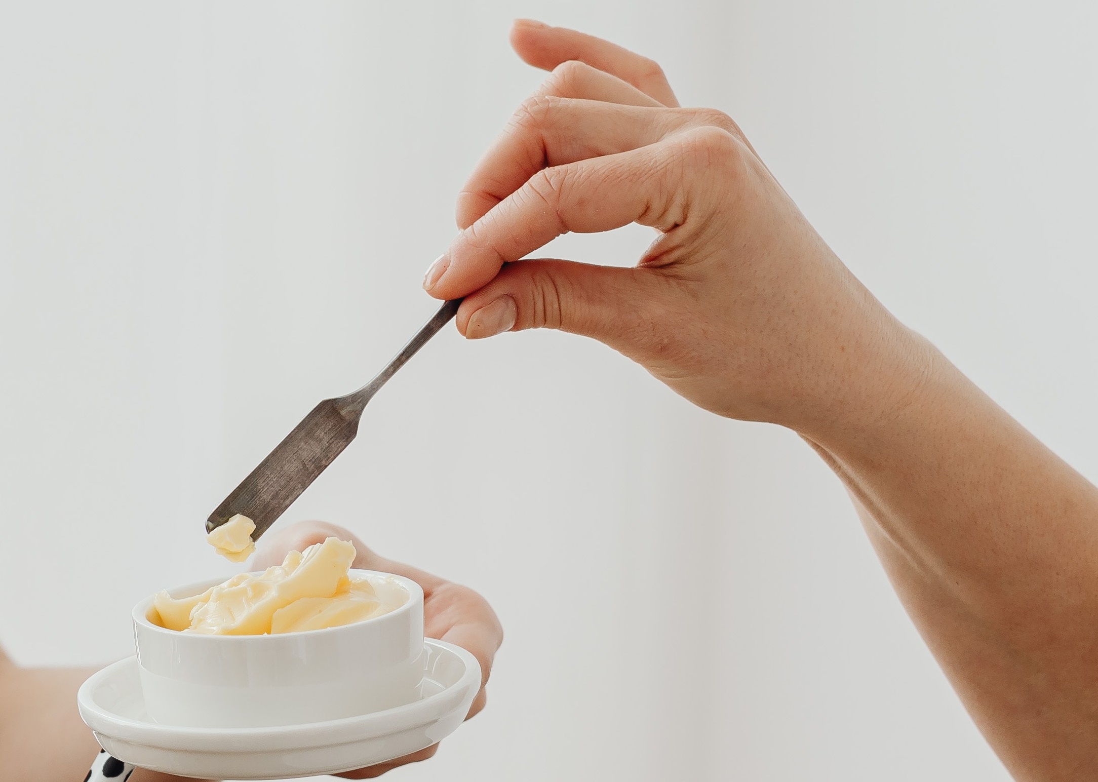 Hand of a woman taking some butter from small white dish.