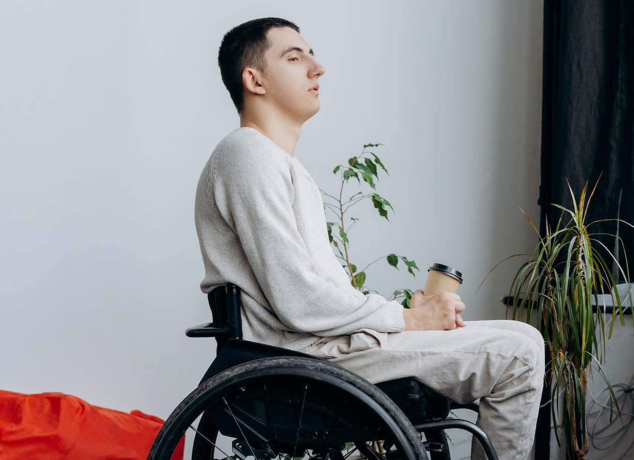 Young man is seating on wheel chair and looking at side.