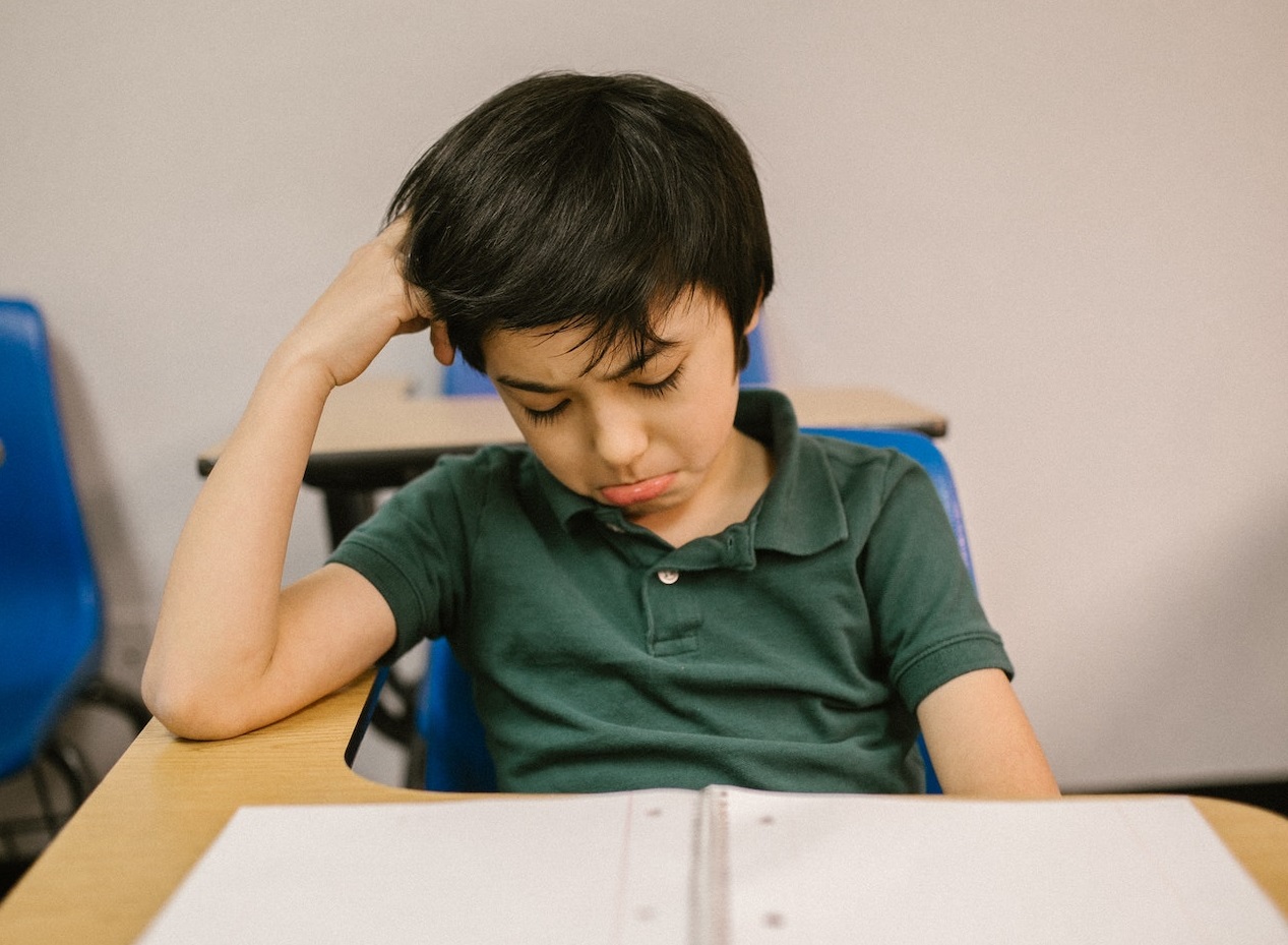 Kid is seating in school bench with sad face.