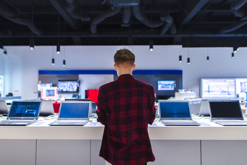 A young man in plaid shirt chooses a laptop in the store