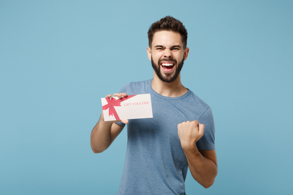 Happy Man holding a coupon in blue t-shirt looking at the camera