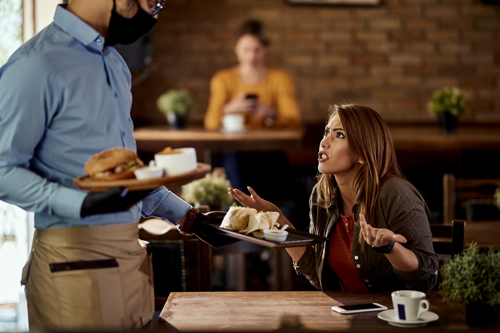 Young woman arguing with a waiter in a restaurant.