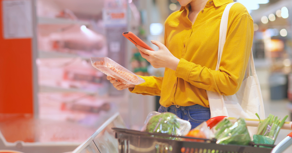 close up of young woman in yellow shirt shopping for meat and scanning barcode