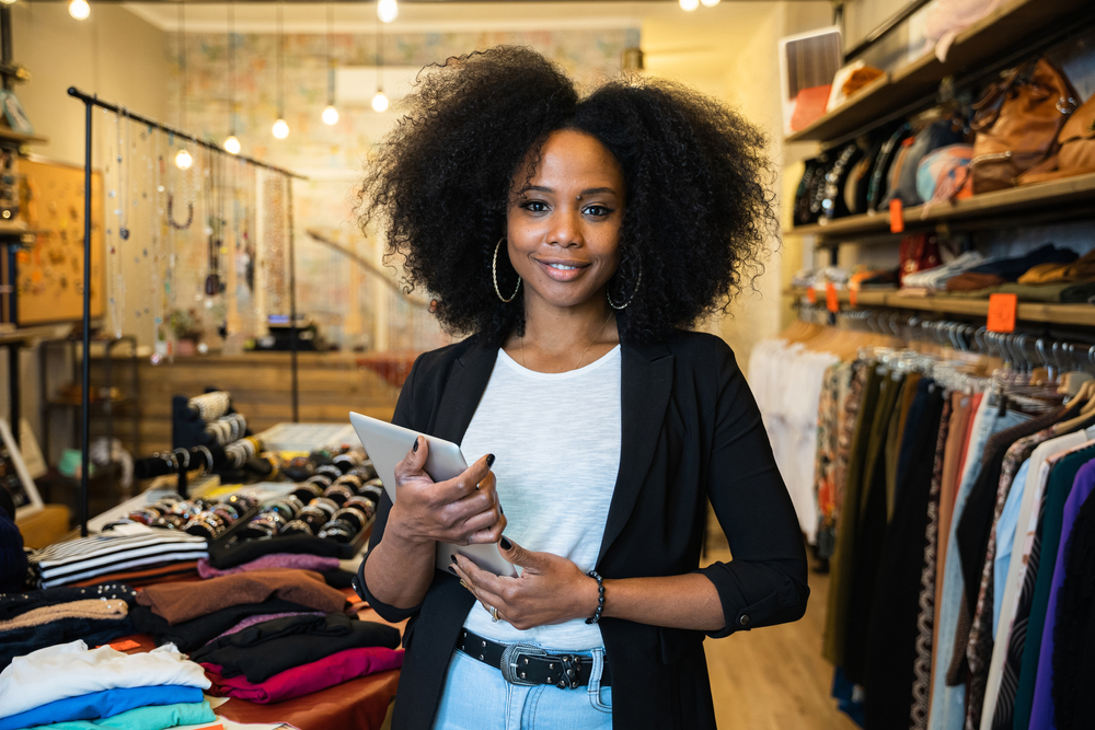 Portrait of the owner of a clothing store at the entrance of the new business with the tablet in hand in black blazer and jeans