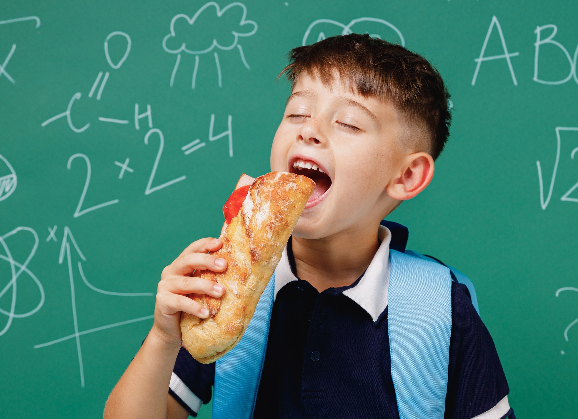 Kid is eating a sandwich in classroom.