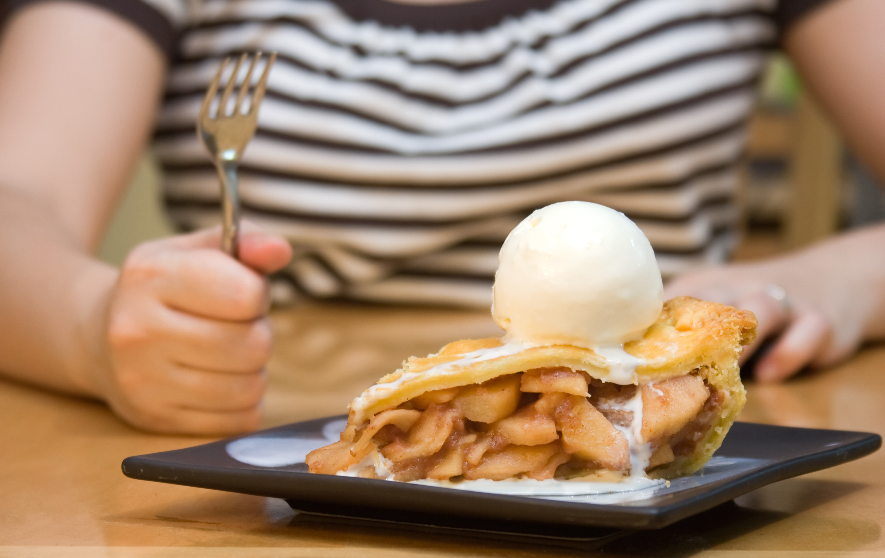 Woman in B&W shirt is holding up fork, ready to eat the apple pie in front of her.