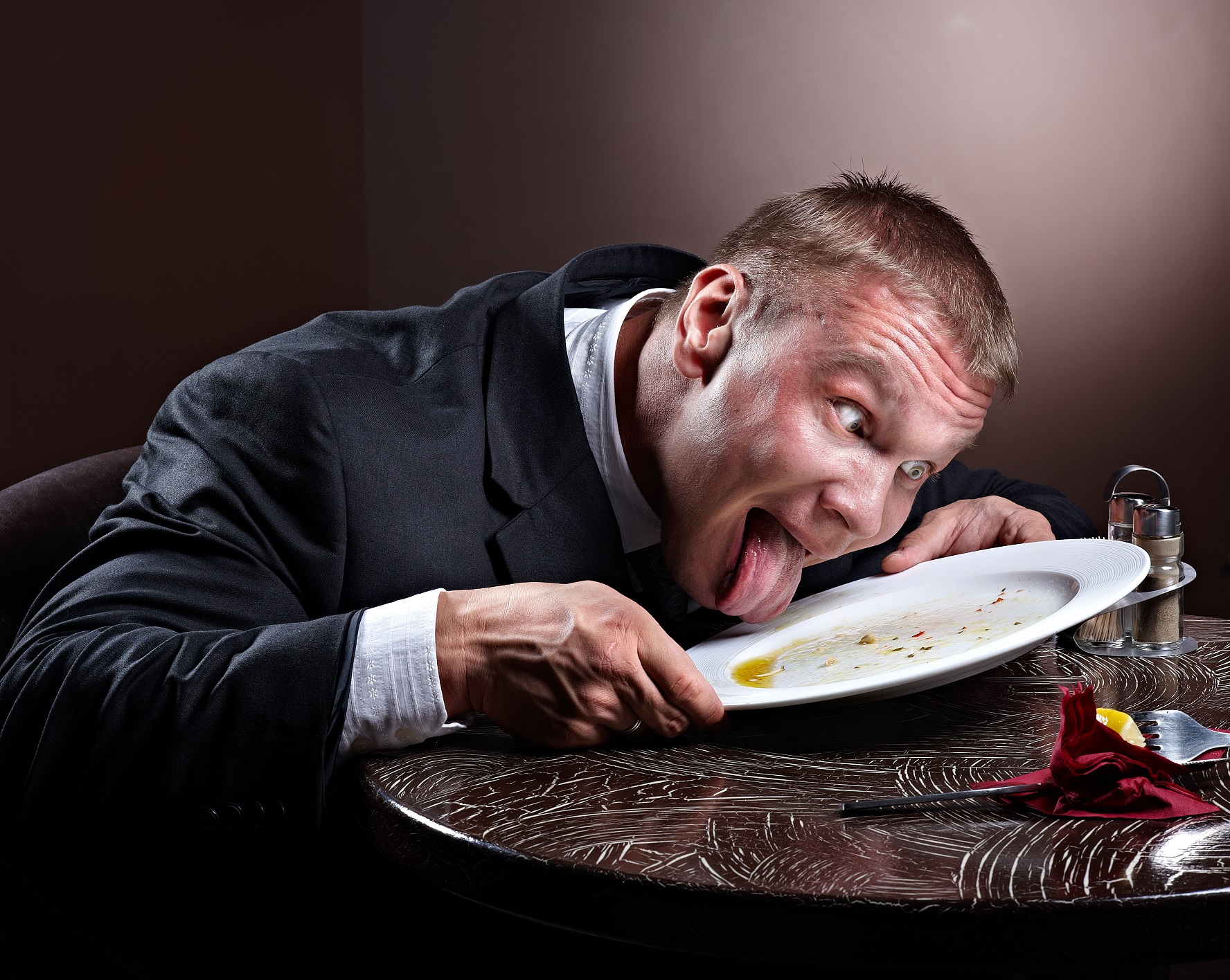 Man wearing suit is licking his plate clean.