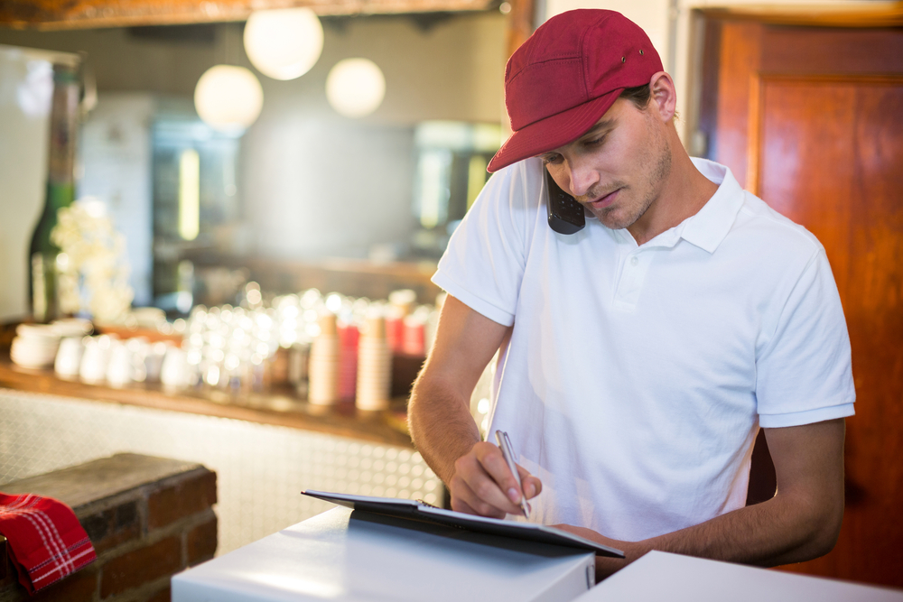 Pizza delivery man in white t-shirt and red hat taking an order over the phone