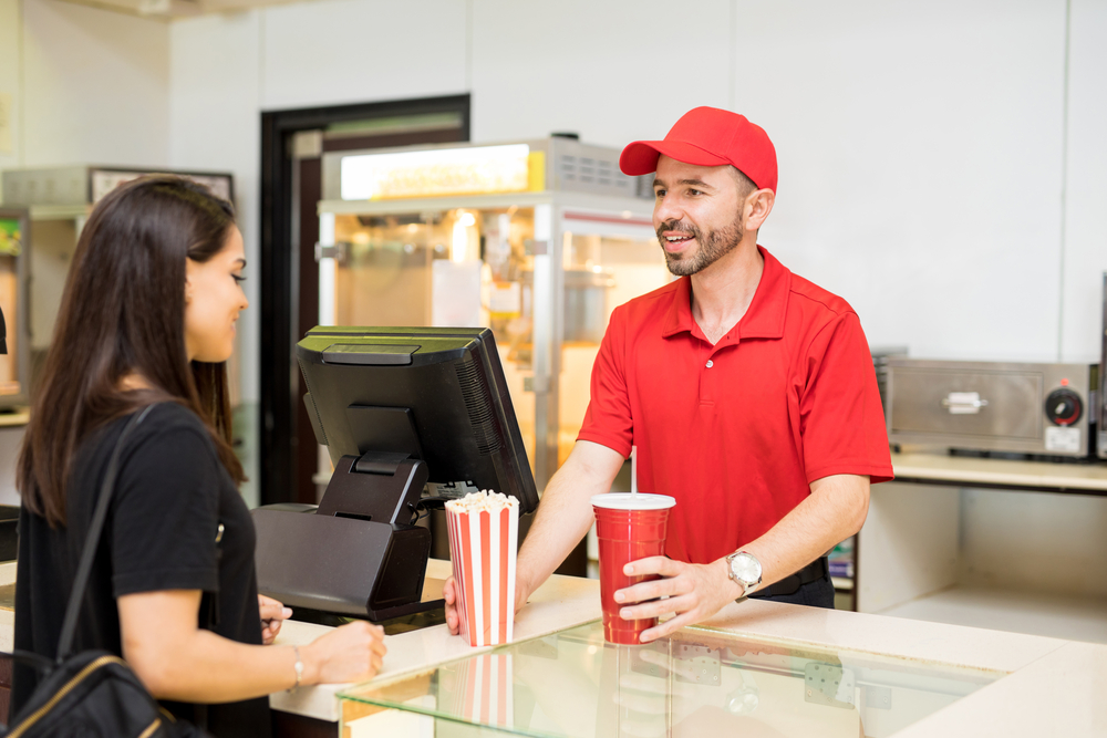 Portrait of a good looking worker in red uniform in a concession food in a movie theater