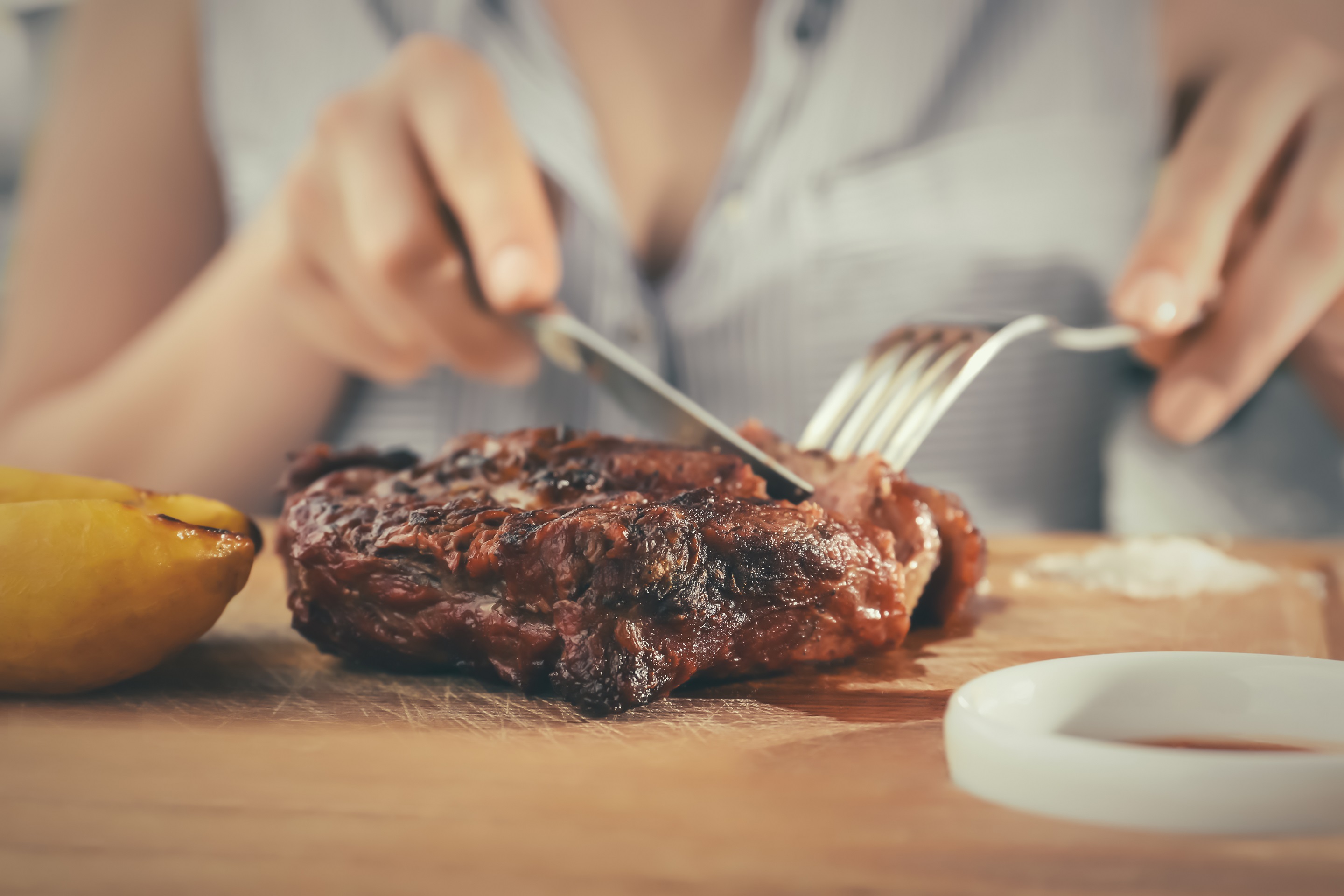 Woman is eating grilled steak on wooden board.
