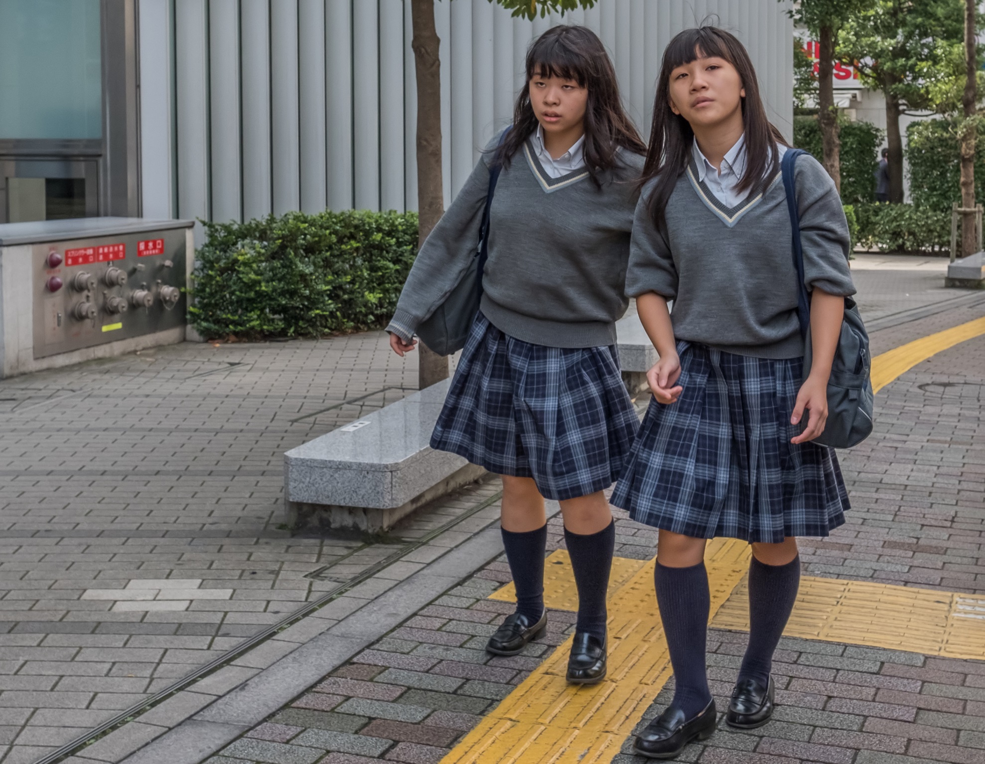 Two young girls in school uniforms and walking on the sidewalk.